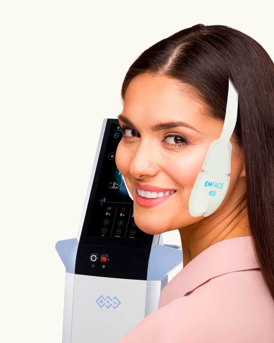 Smiling patient beside the EMFACE device with a facial applicator in place
